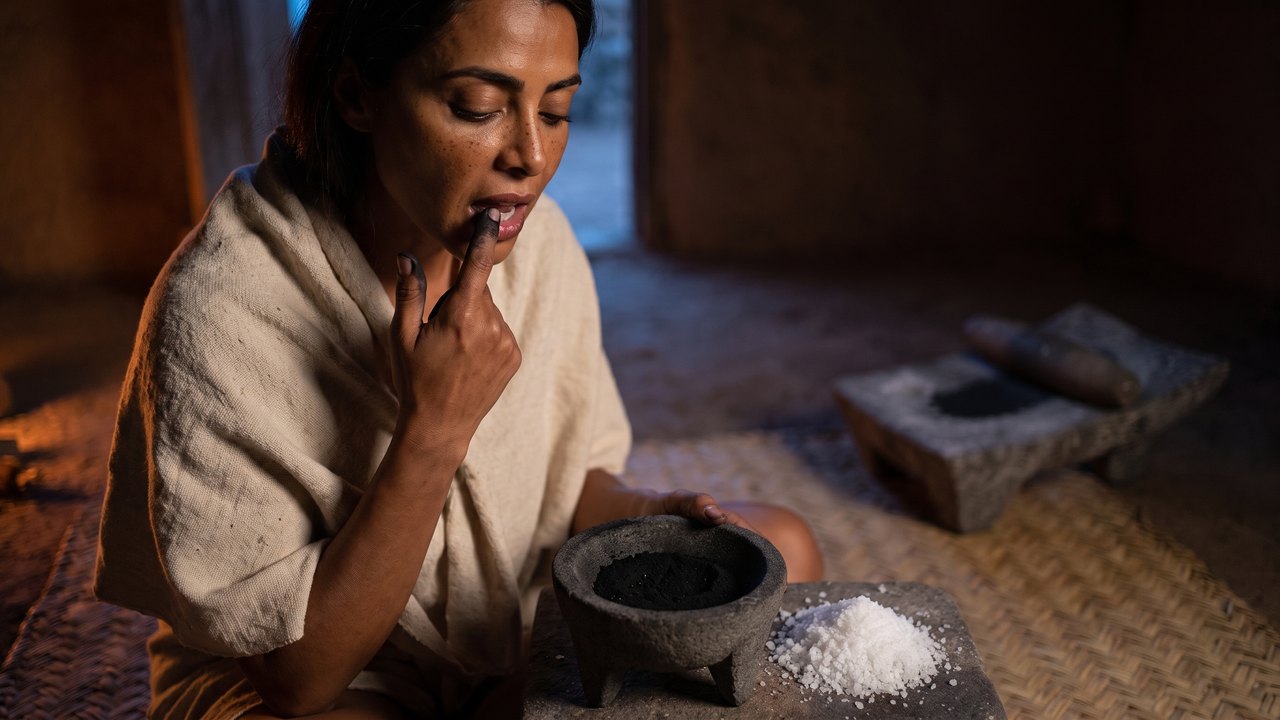 Is charcoal toothpaste good for your teeth — before sunrise in a house in Tenochtitlan a Mexica woman presses a charcoal-blackened fingertip along her own gum, a three-legged basalt bowl of black charcoal dust and a heap of white salt on the stone beside her