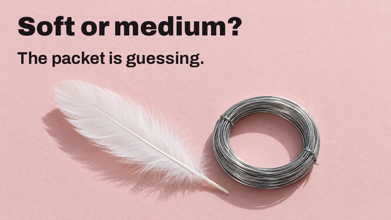 Soft or medium? The packet is guessing. Seen from above: a soft white feather beside a tight coil of stiff steel wire on pale pink paper.