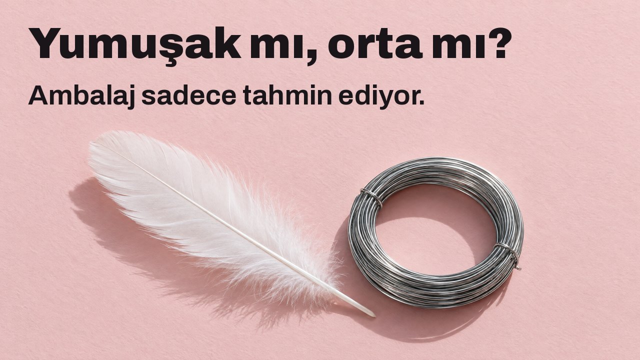 Yumuşak mı, orta mı? Ambalaj sadece tahmin ediyor. Yukarıdan: soluk pembe kâğıt üzerinde yumuşak beyaz bir tüy ve sıkı sarılmış sert çelik tel.