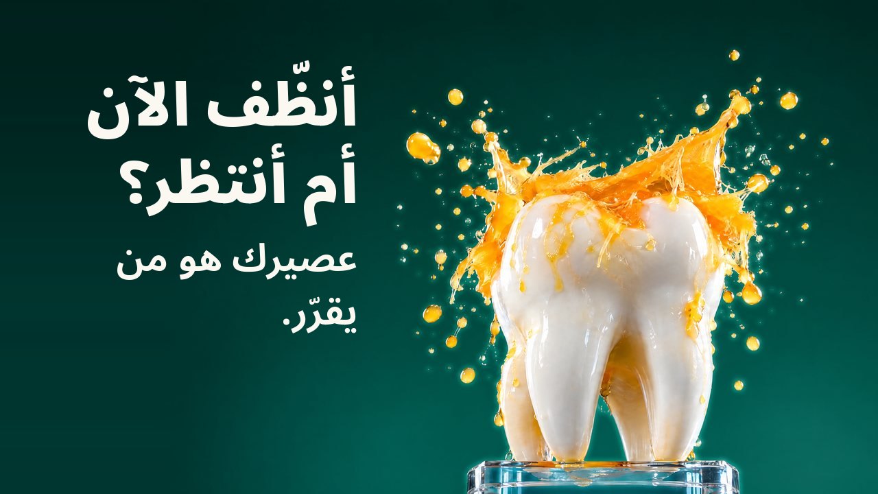 أنظّف الآن أم أنتظر؟ عصيرك هو من يقرّر. مجسّم سنّ أبيض على قاعدة زجاجية تحت رذاذ من عصير البرتقال متجمّد في الهواء، أمام خلفية خضراء داكنة.