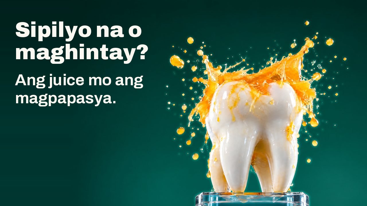 Sipilyo na o maghintay? Ang juice mo ang magpapasya. Isang puting eskultura ng ngipin sa basong patungan, sa ilalim ng talsik ng orange juice na nakahinto sa ere, sa malalim na berdeng background ng studio.