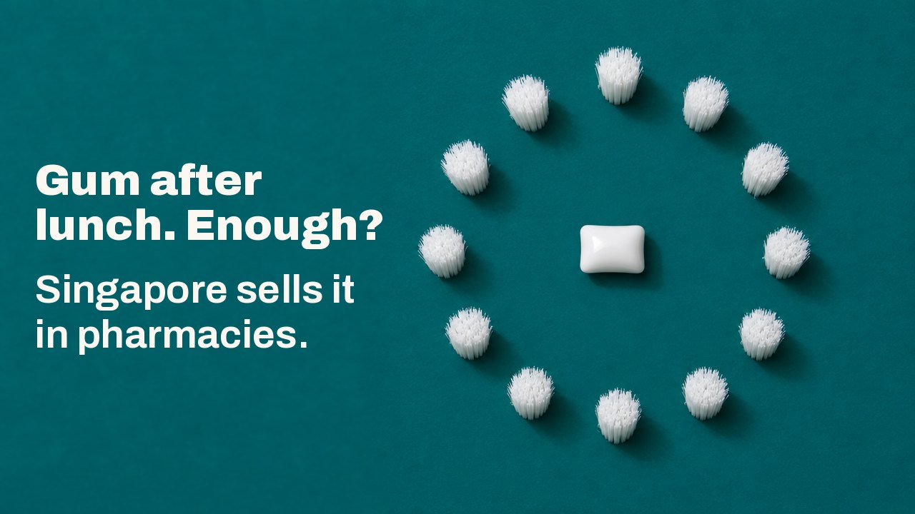 Gum after lunch. Enough? Singapore sells it in pharmacies. Seen from directly above on a deep teal ground: one white pellet of chewing gum lies at the centre of a perfect ring of white bristle tufts, like a clock face without hands.