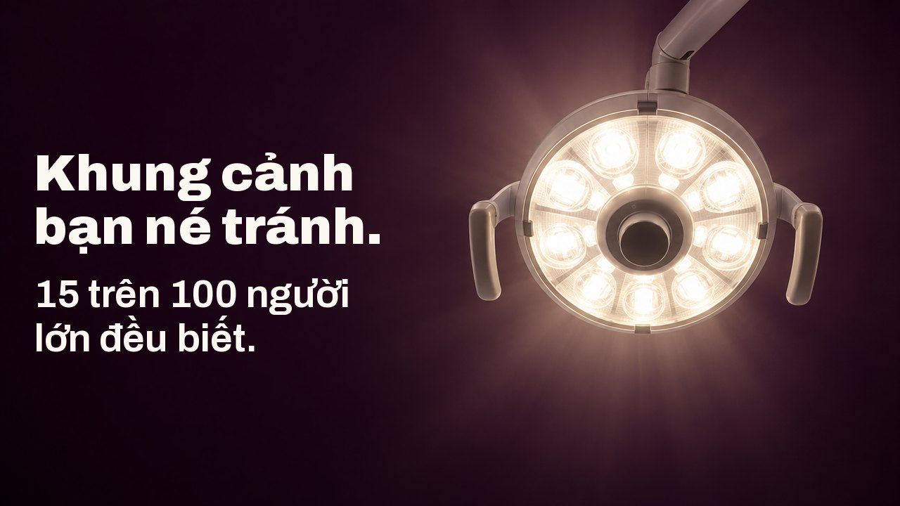 Khung cảnh bạn né tránh. 15 trên 100 người lớn đều biết. Khung cảnh nhìn thẳng lên từ ghế nha khoa: một chiếc đèn nha khoa tròn tỏa ánh sáng trắng ấm trên nền trần nhà màu tím cà đậm.