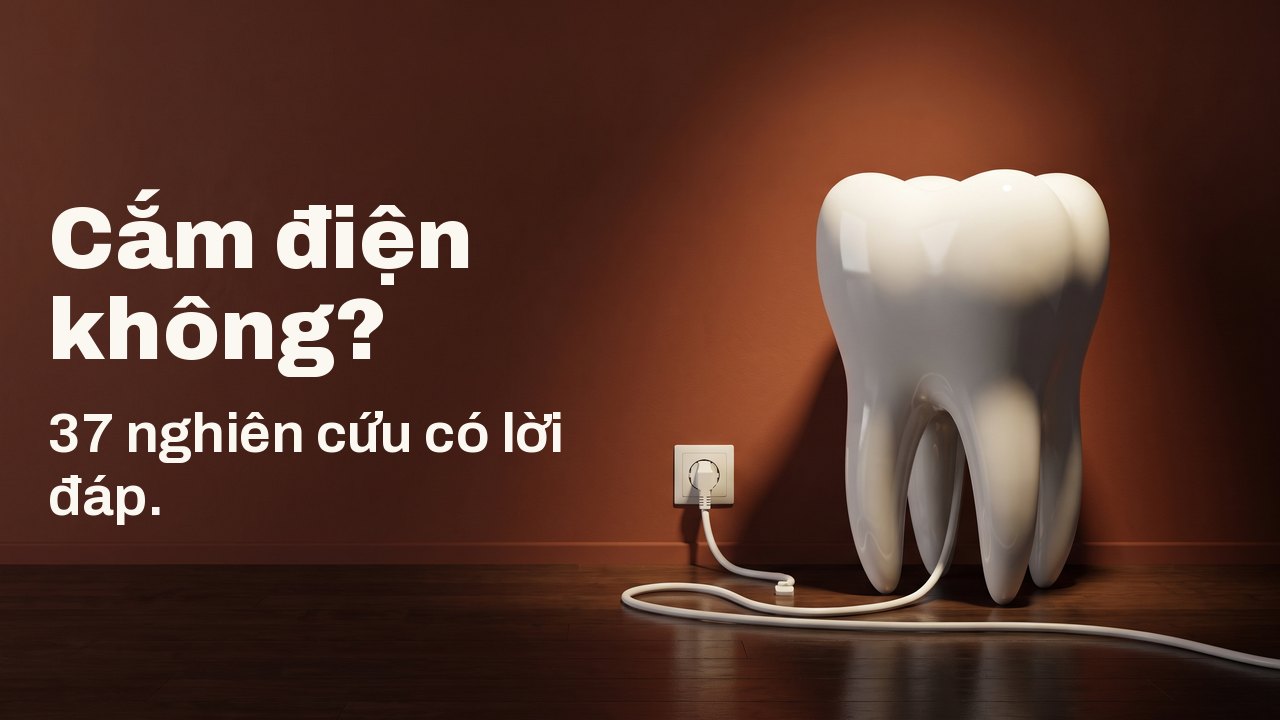 Cắm điện không? 37 nghiên cứu có lời đáp. Một mô hình răng bằng sứ trắng trên sàn gỗ, trước bức tường màu đất nung, sợi dây trắng của nó cắm vào ổ điện trên tường.