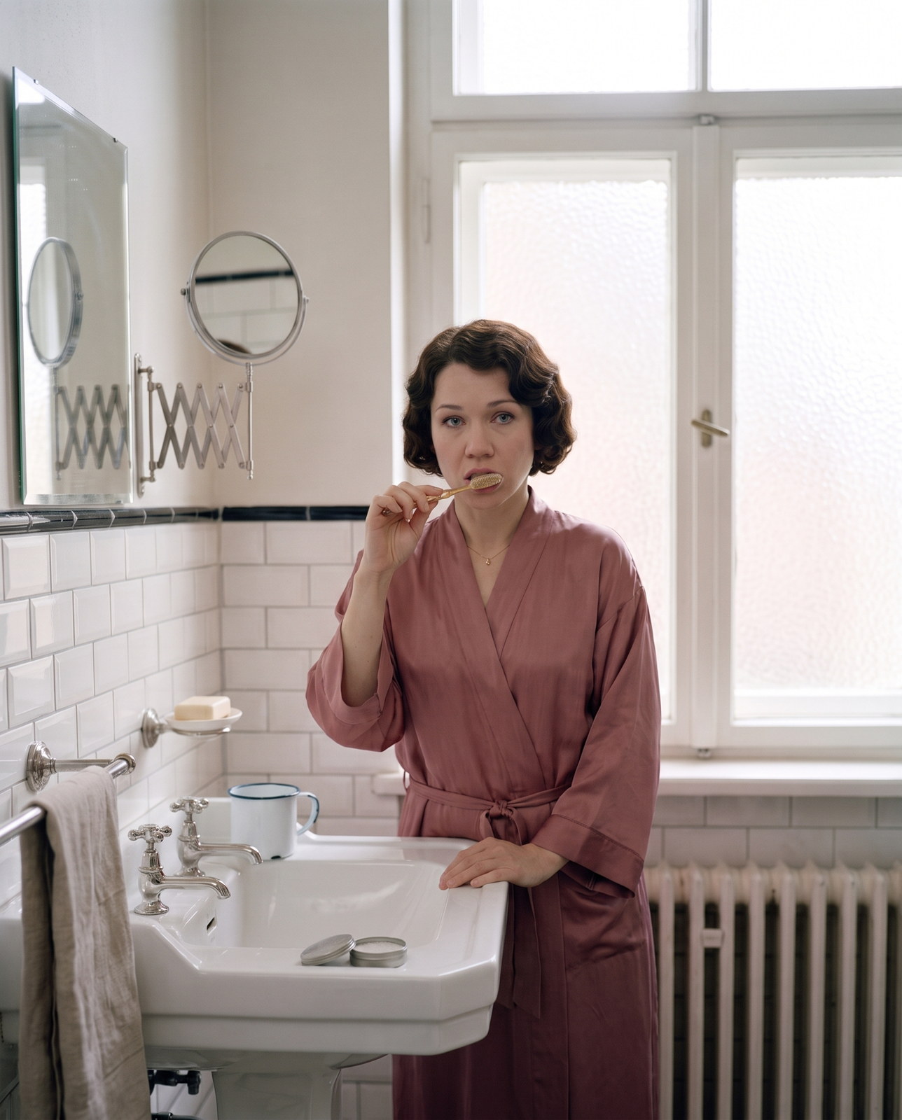 The future of oral health — a woman with a 1920s finger-waved bob brushes her teeth with a celluloid brush and tooth powder at a pedestal basin in a 1925 Berlin bathroom