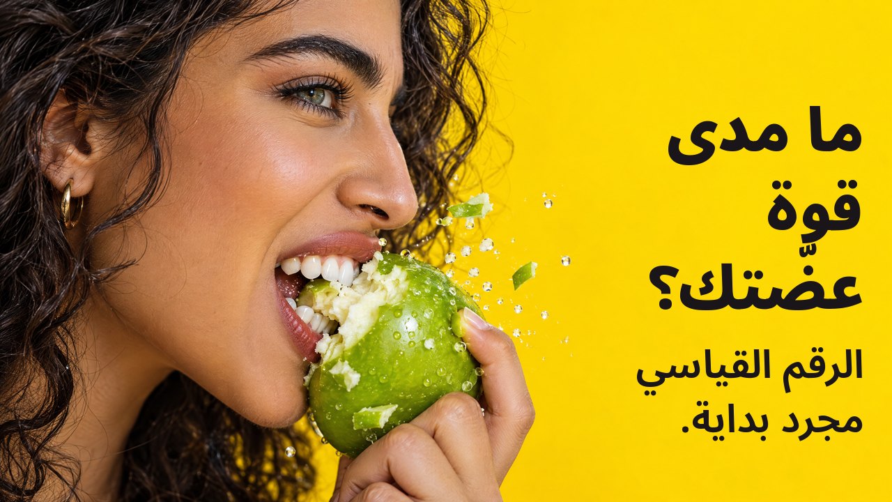 ما مدى قوة عضّتك؟ الرقم القياسي مجرد بداية. لقطة جانبية قريبة لامرأة تقضم بقوة تفاحة خضراء مقرمشة وتتطاير قطعها، على خلفية صفراء زاهية.