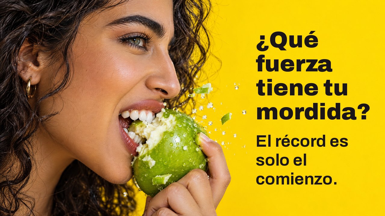 ¿Qué fuerza tiene tu mordida? El récord es solo el comienzo. Primer plano de perfil de una mujer que muerde con fuerza una manzana verde crujiente, con trozos volando, sobre amarillo intenso.