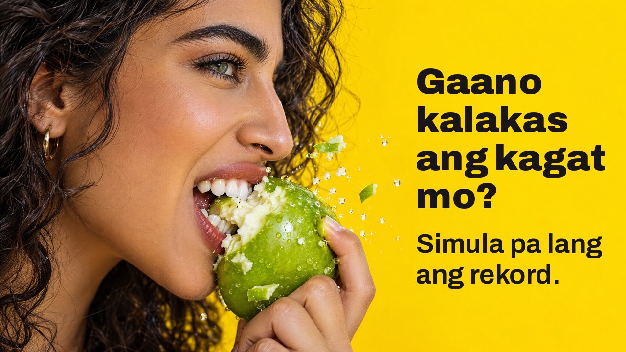 Gaano kalakas ang kagat mo? Simula pa lang ang rekord. Malapitang kuha mula sa gilid ng babaeng mariing kumakagat sa malutong na berdeng mansanas, lumilipad ang mga piraso, sa matingkad na dilaw.