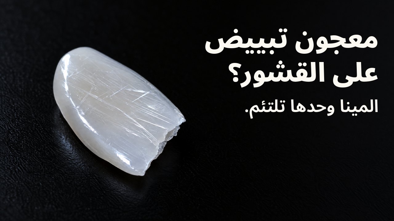 معجون تبييض على القشور؟ المينا وحدها تلتئم. تحت ضوء جانبي: شظية خزفية رقيقة لامعة تشبه القشرة، تعبرها خدوش دقيقة، على الأسود.