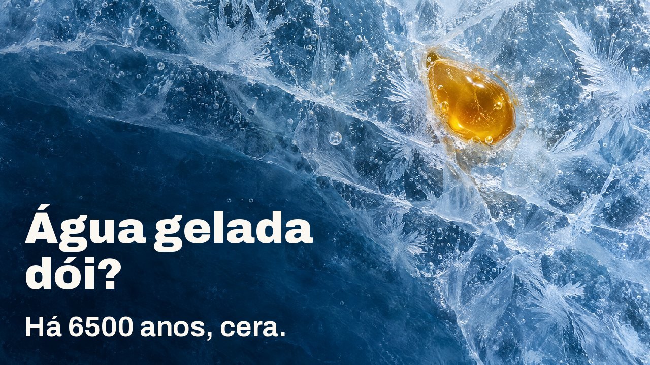 Água gelada dói? Há 6500 anos, cera. Visto de cima: uma gota de cera de abelha dourada presa em gelo azul rachado, com flores de geada e bolhas de ar.