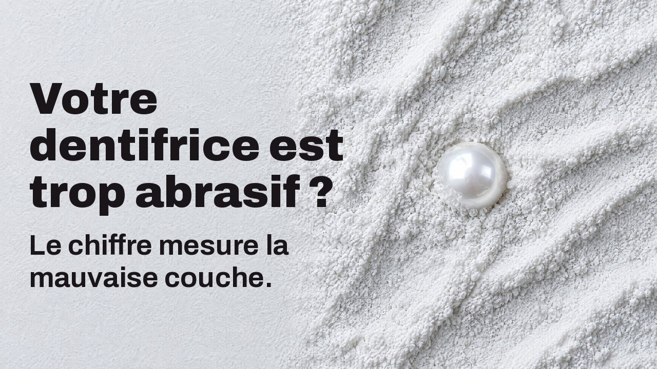Votre dentifrice est trop abrasif ? Le chiffre mesure la mauvaise couche. Vu d’en haut : une perle brillante à demi enfouie dans une fine poudre abrasive blanche.