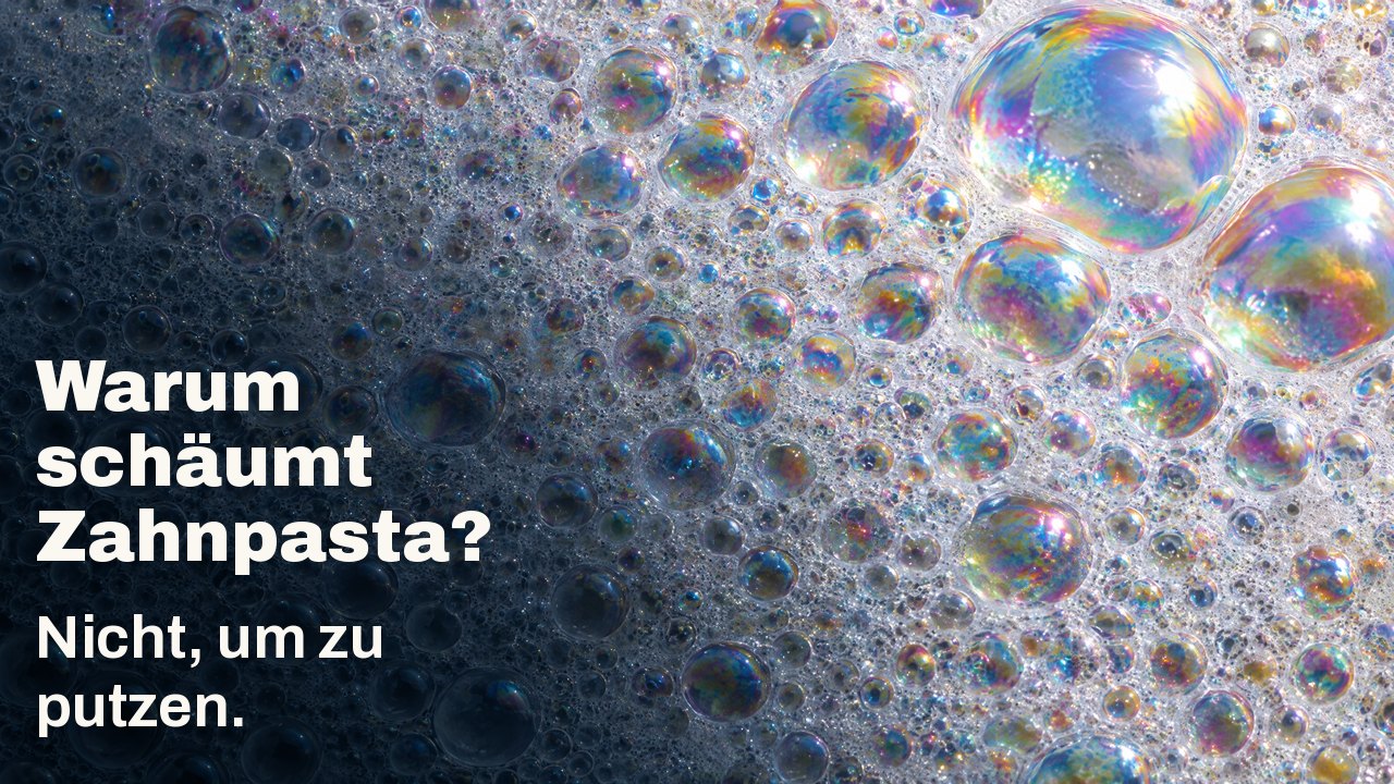 Warum schäumt Zahnpasta? Nicht, um zu putzen. Makro von weißem Schaum: unzählige kleine Bläschen mit schillerndem Regenbogenfilm, einige große fangen das Licht.