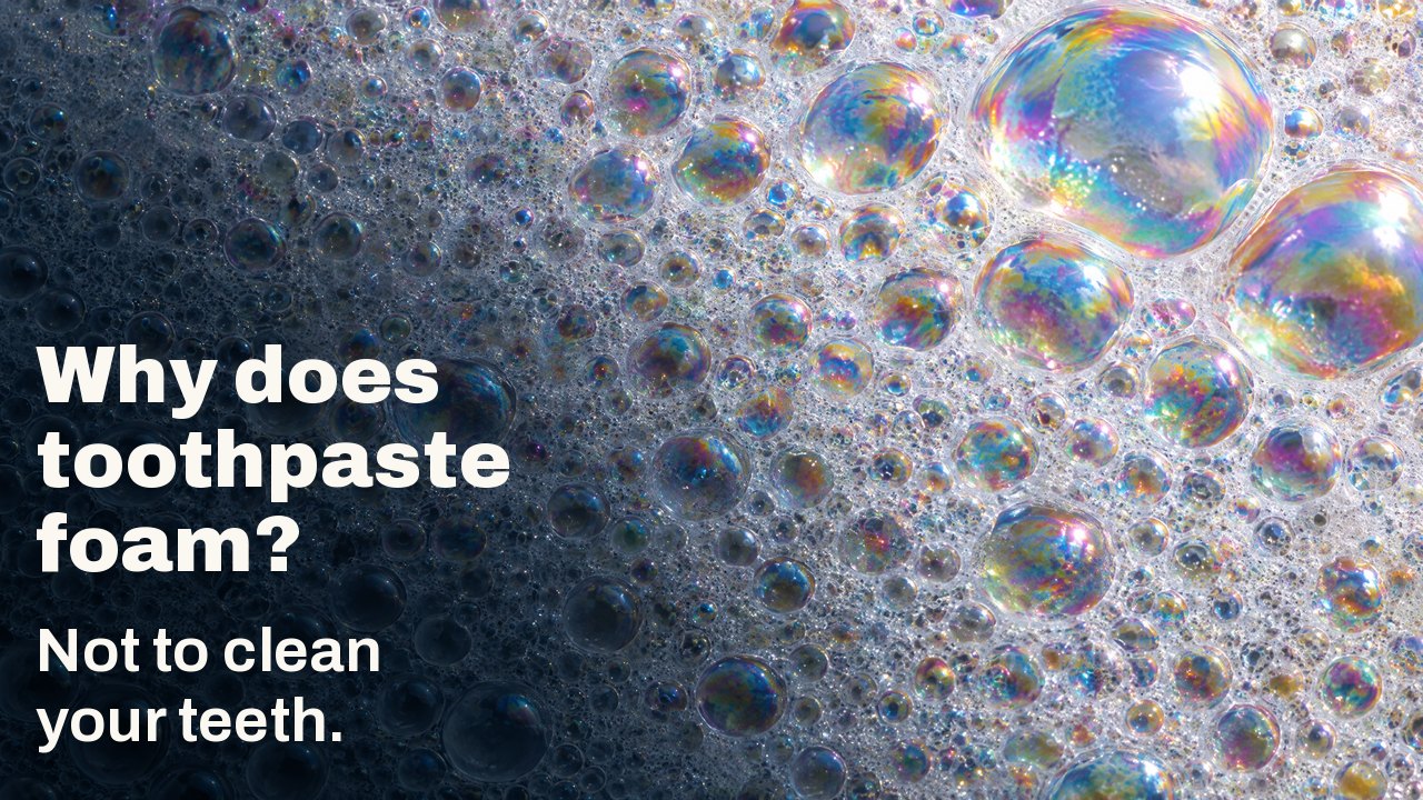 Why does toothpaste foam? Not to clean your teeth. Macro of white foam: countless small bubbles with iridescent rainbow film, a few large bubbles catching the light.