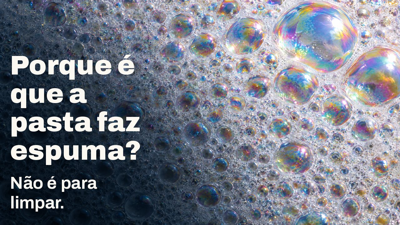 Porque é que a pasta faz espuma? Não é para limpar. Macro de espuma branca: inúmeras bolhas pequenas com película iridescente, algumas grandes a apanhar a luz.