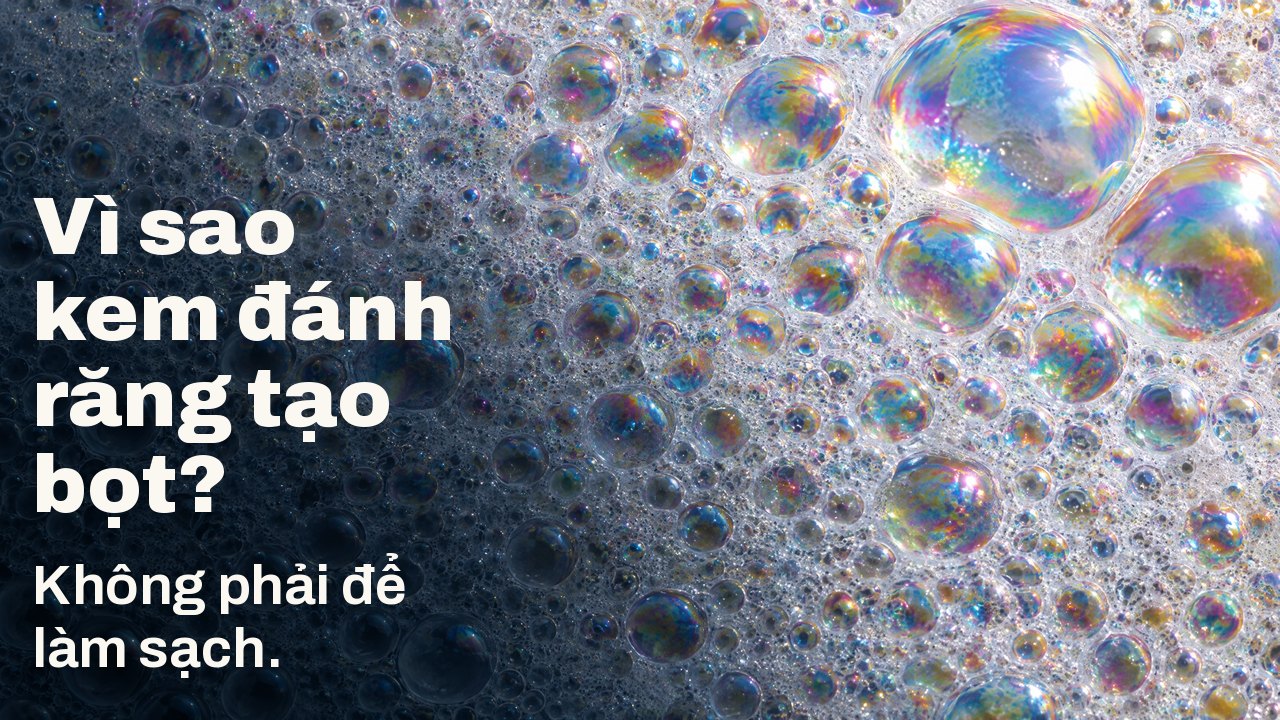 Vì sao kem đánh răng tạo bọt? Không phải để làm sạch. Macro bọt trắng: vô số bọt nhỏ phủ màng óng ánh cầu vồng, vài bong bóng lớn bắt sáng.