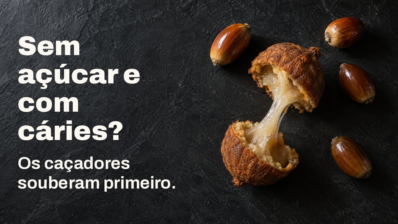 Sem açúcar e com cáries? Os caçadores souberam primeiro. Visto de cima: bolotas descascadas e um bolo de bolota partido com um fio pegajoso de amido entre as metades, sobre ardósia escura.