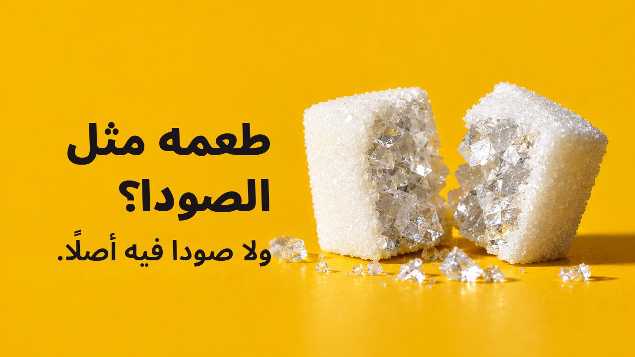 طعمه مثل الصودا؟ ولا صودا فيه أصلًا. لقطة قريبة جدًا من مستوى الطاولة على خلفية صفراء دافئة بلون الزعفران: مكعب سكر أبيض مشطور نصفين، وفي داخله لا سكر، بل بلورات ملح كبيرة لامعة كالزجاج.