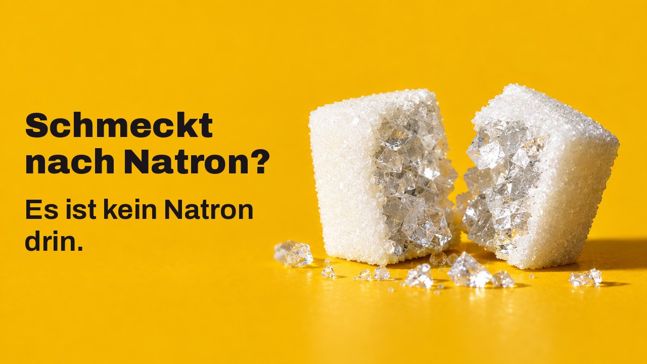 Schmeckt nach Natron? Es ist kein Natron drin. Extreme Nahaufnahme auf Tischhöhe vor warmem Safrangelb: Ein weißes Zuckerstück, in zwei Hälften gebrochen, und darin kein Zucker, sondern große, glasige Salzkristalle.