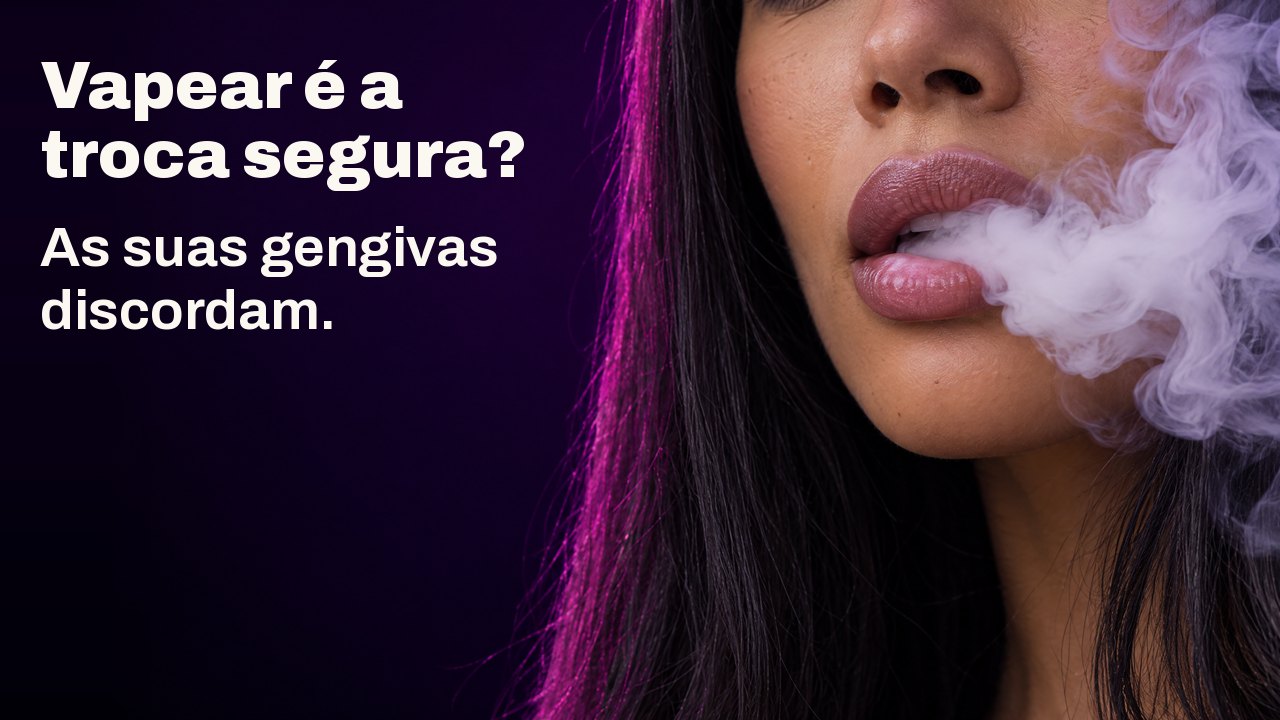 Vapear é a troca segura? As suas gengivas discordam. Grande plano dos lábios de uma mulher a exalar uma nuvem densa de vapor branco, sobre violeta escuro.